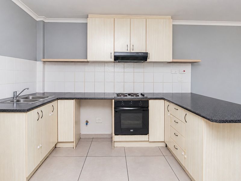 A clean, functional kitchen featuring light wood-tone cabinetry, dark laminate countertops, built-in oven, electric hob, and tiled flooring.
