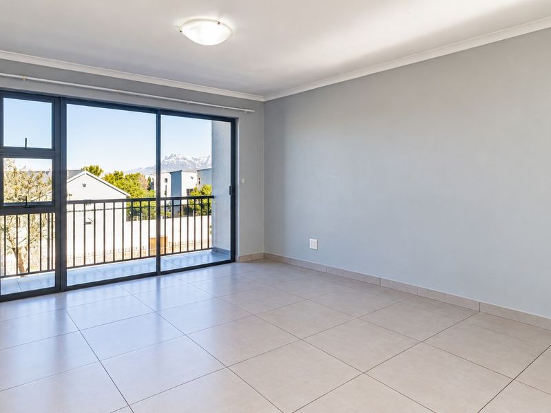 A bright, empty living room featuring neutral tiled flooring, a large sliding glass door leading to a balcony, and clean, modern finishes.