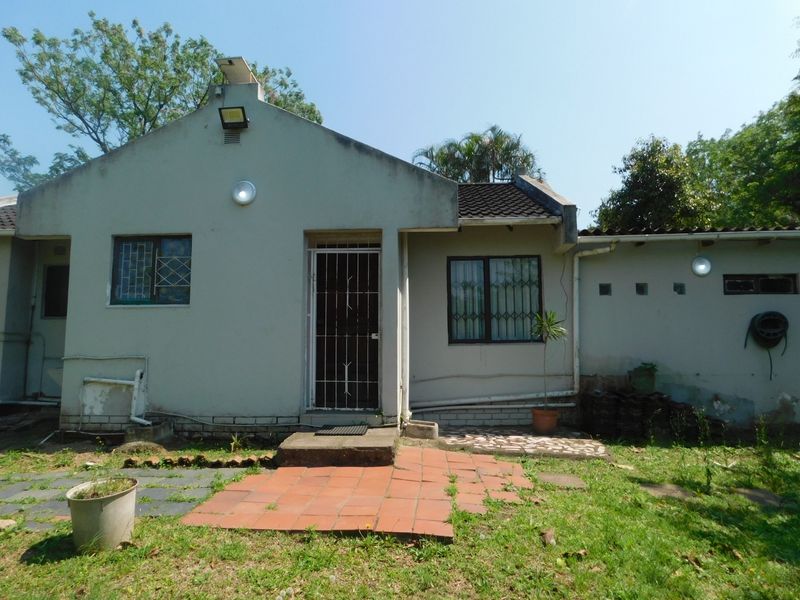 Rear exterior view of a townhouse featuring a tiled roof, security bars on windows, and a small paved patio area requiring maintenance.