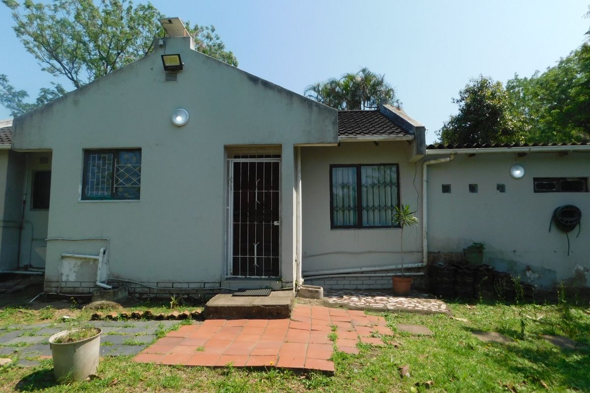 Rear exterior view of a townhouse featuring a tiled roof, security bars on windows, and a small paved patio area requiring maintenance.