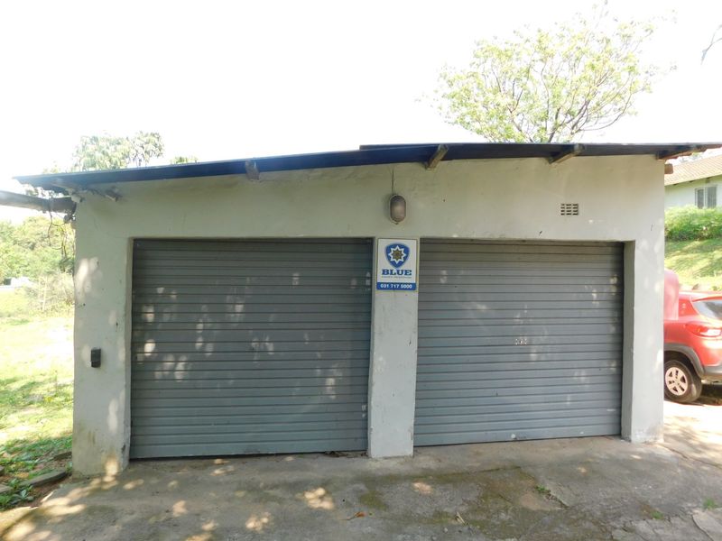 A detached double garage featuring roller doors, an external security alarm sign, and a concrete driveway in need of maintenance.