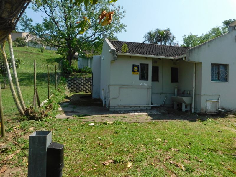 Rear view of the townhouse featuring a paved patio area, external utility sink, and security features, set against a grassy backyard.