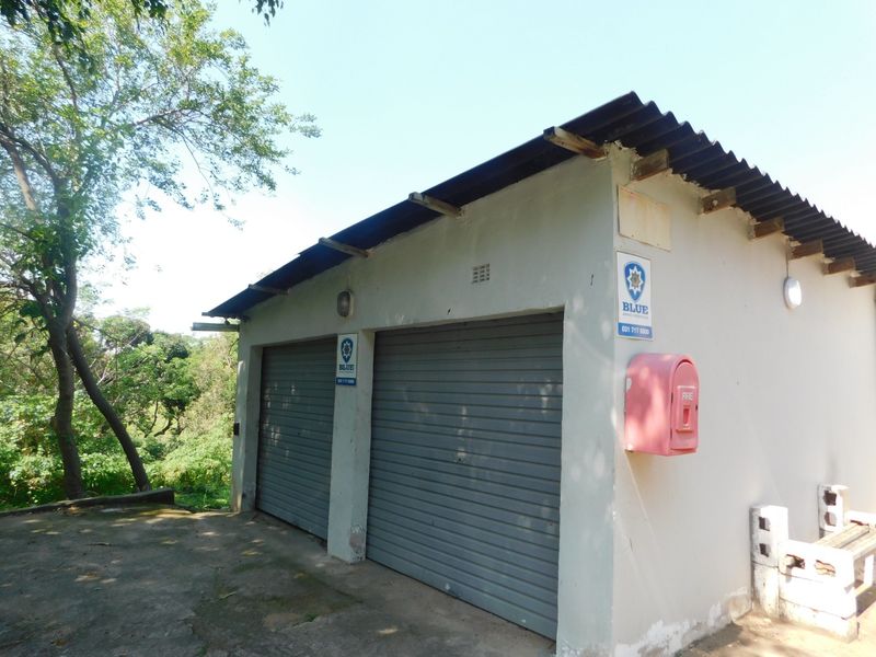 A detached double garage featuring roller doors, a corrugated roof, and an external fire hose reel, situated on a concrete driveway.