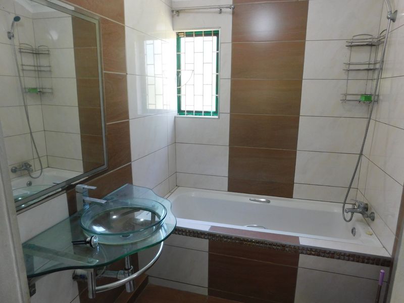 A functional bathroom featuring a bathtub, a modern glass vessel sink, and contrasting brown and white wall tiling.