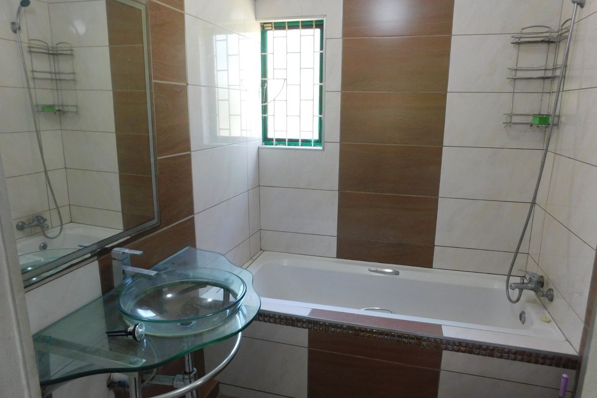 A functional bathroom featuring a bathtub, a modern glass vessel sink, and contrasting brown and white wall tiling.