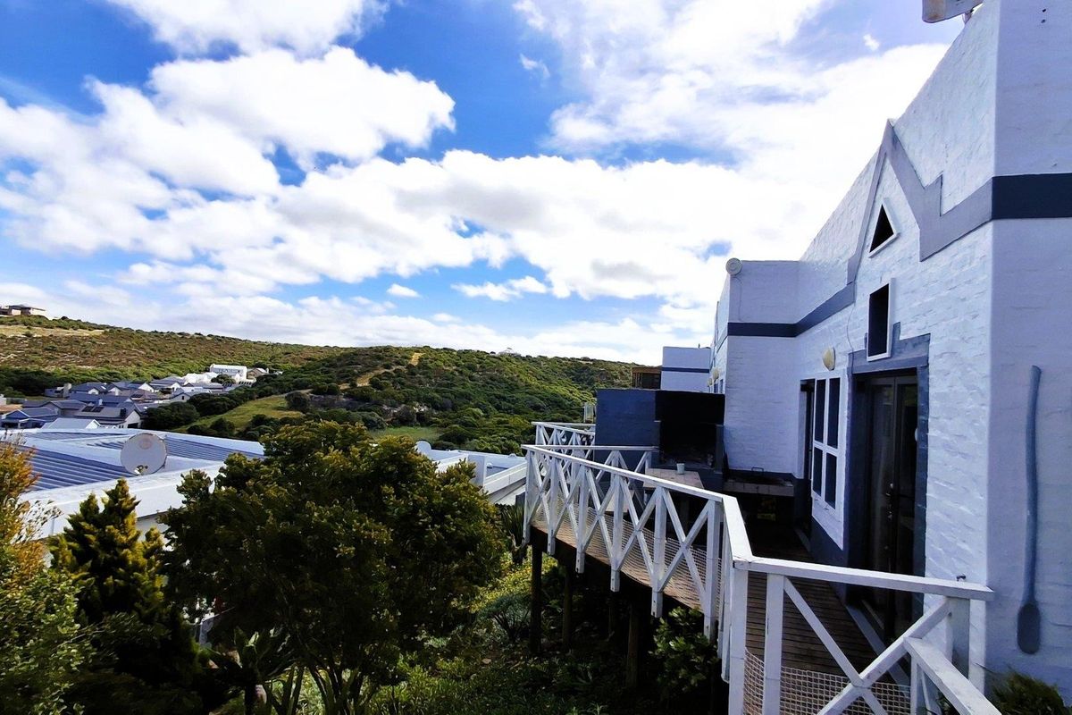 Rear exterior view of the apartment featuring a wooden deck, built-in braai area, and scenic hillside views.