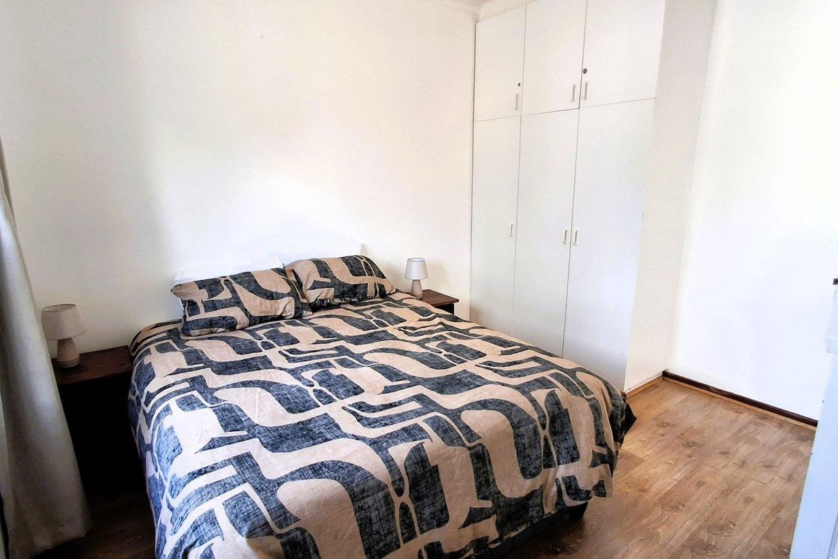 A functional bedroom featuring built-in cupboards and laminate flooring, providing a clean and neutral space.
