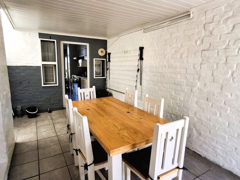 A covered patio area featuring tiled flooring, painted brick walls, and a tongue and groove ceiling, providing a functional outdoor dining space.