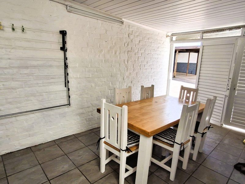 A covered patio area featuring tiled flooring, a painted brick wall, and a wall-mounted drying rack, providing a functional outdoor space.