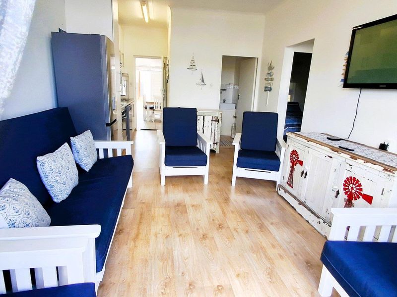A bright living room area featuring light-toned laminate flooring, providing a functional space that connects to the kitchen and other rooms.