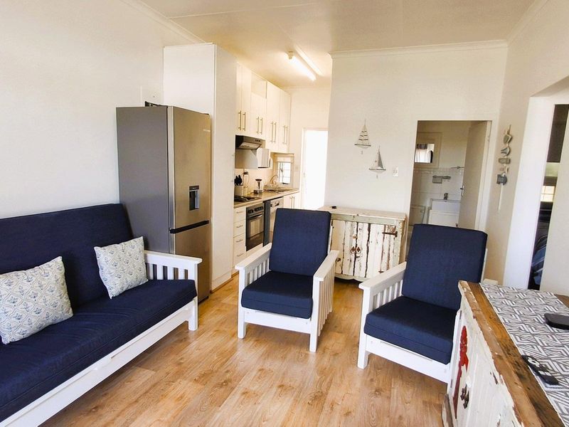 Open-plan living area featuring laminate flooring and a functional kitchen with built-in cabinetry, oven, and extractor fan, leading to an adjacent bathroom.