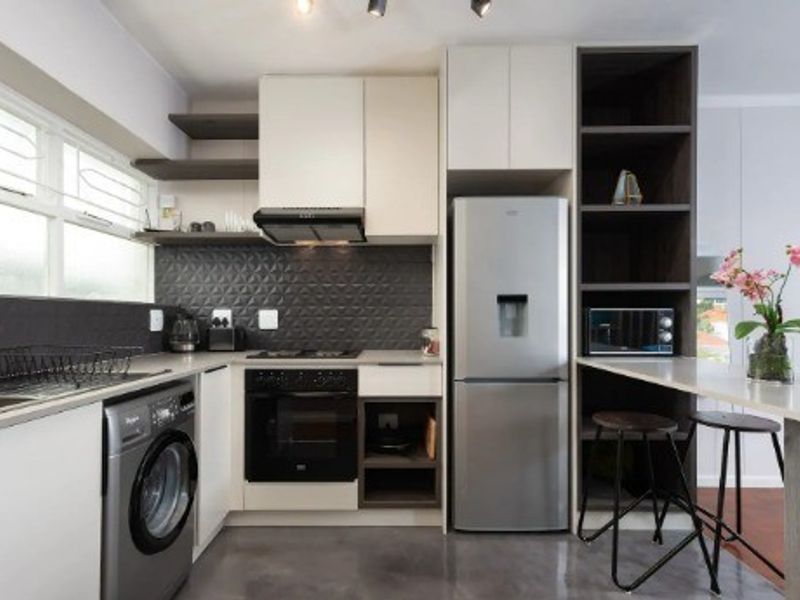 Modern kitchen featuring sleek cabinetry, a textured tile backsplash, built-in oven and hob, integrated breakfast bar, and polished concrete flooring.