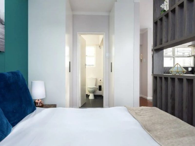 A well-maintained bedroom featuring built-in cupboards and a decorative partition shelving unit, with a view through to an adjacent bathroom.