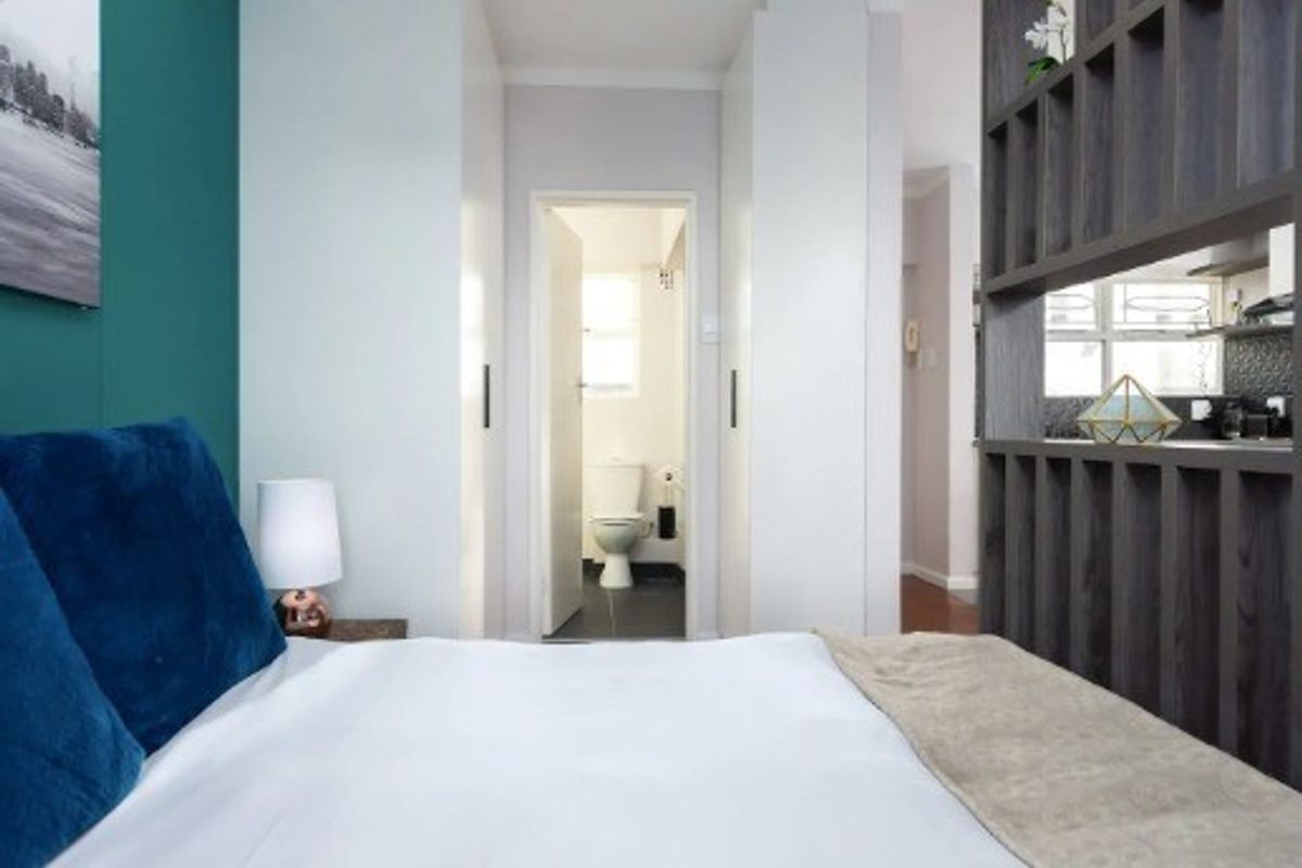 A well-maintained bedroom featuring built-in cupboards and a decorative partition shelving unit, with a view through to an adjacent bathroom.