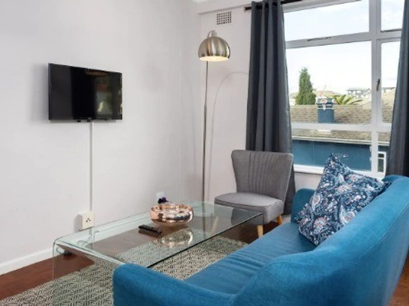A bright living room featuring parquet flooring and a large window providing natural light and an exterior view.