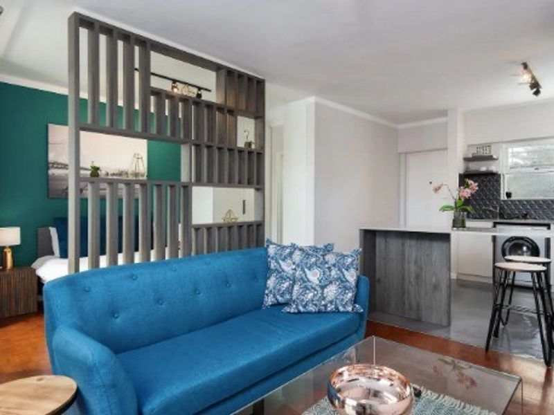 An open-plan living area featuring a modern wooden room divider, a functional kitchen with an island, and warm hardwood flooring throughout.