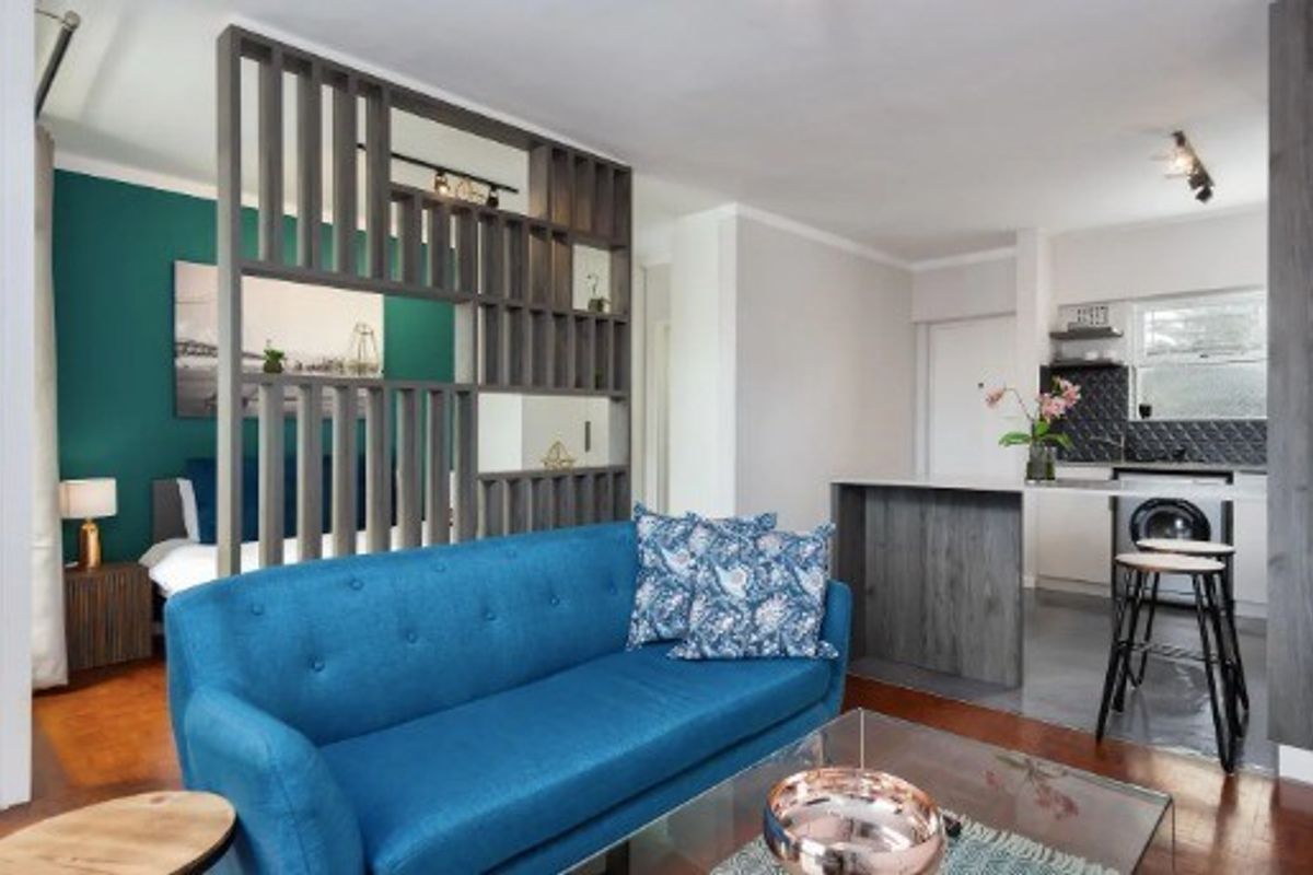 An open-plan living area featuring a modern wooden room divider, a functional kitchen with an island, and warm hardwood flooring throughout.