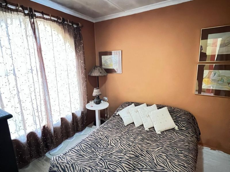 A bedroom featuring terracotta-toned walls and a large window with sheer curtains. The ceiling shows visible signs of staining.