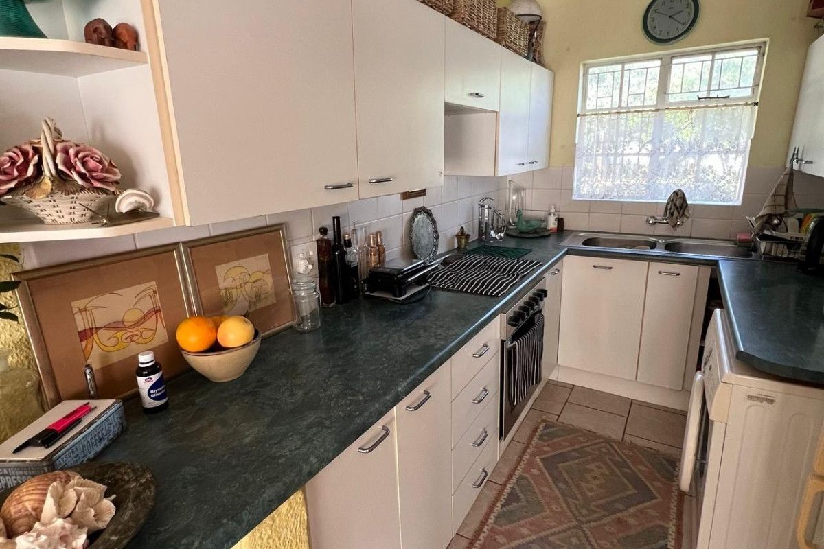 A functional kitchen featuring white cabinetry, dark laminate countertops, a double basin sink, and tiled flooring with a classic backsplash.