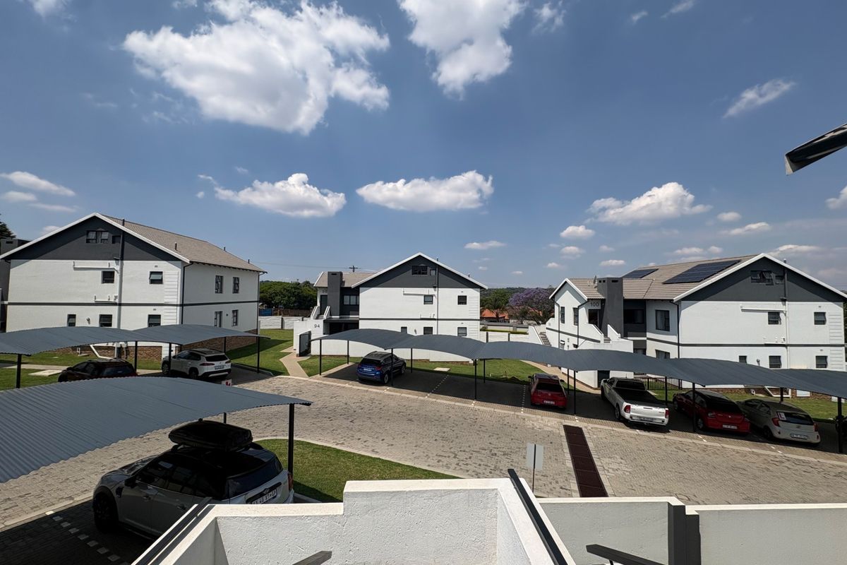 An elevated view of a residential apartment complex featuring paved parking areas with covered carports and modern multi-story building facades.