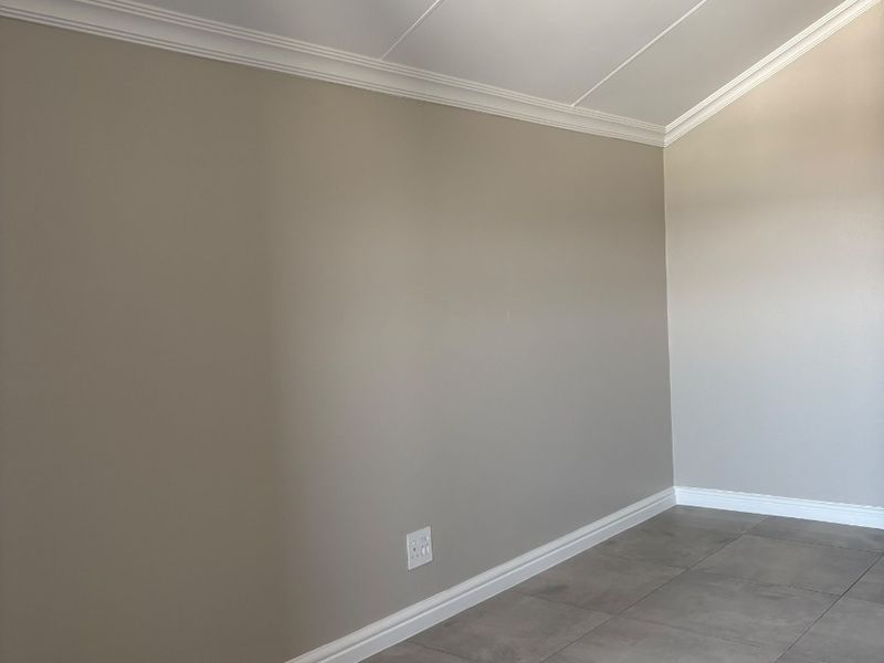 A clean, empty bedroom featuring neutral painted walls, crown molding, baseboards, and modern grey floor tiles.