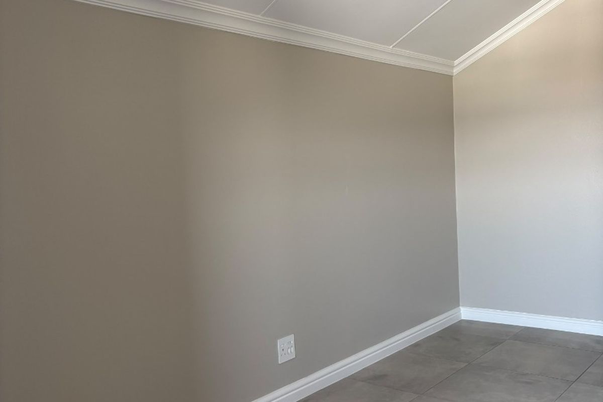 A clean, empty bedroom featuring neutral painted walls, crown molding, baseboards, and modern grey floor tiles.