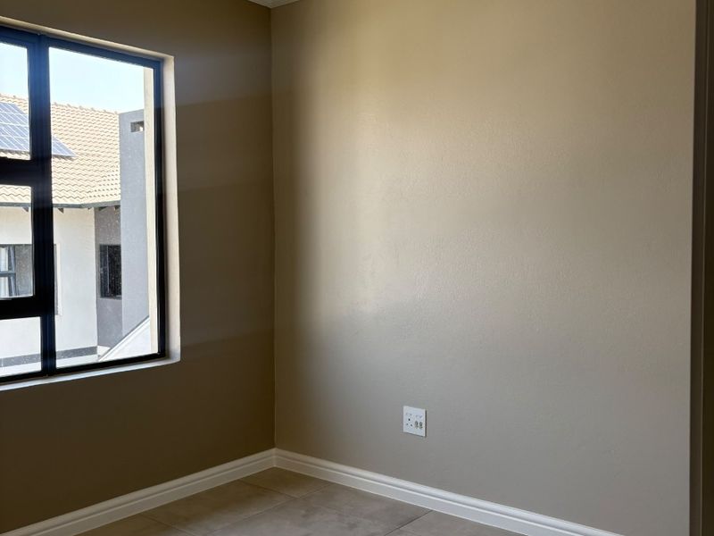 A clean, empty bedroom featuring neutral wall paint, large aluminium-framed windows, and modern tiled flooring with neat skirting and coving details.