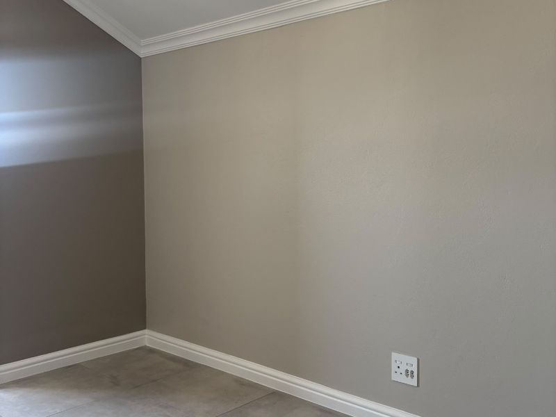 A clean, empty bedroom featuring neutral painted walls, crown molding, baseboards, and modern tiled flooring.