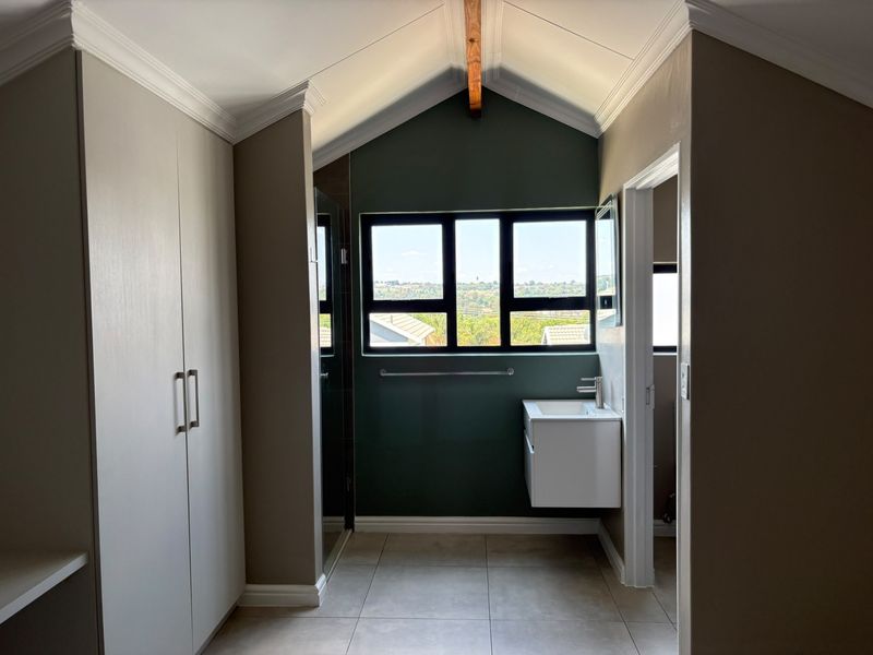 Modern bathroom featuring a floating vanity, built-in cupboards, vaulted ceiling with exposed beam, and large windows offering natural light and scenic views.