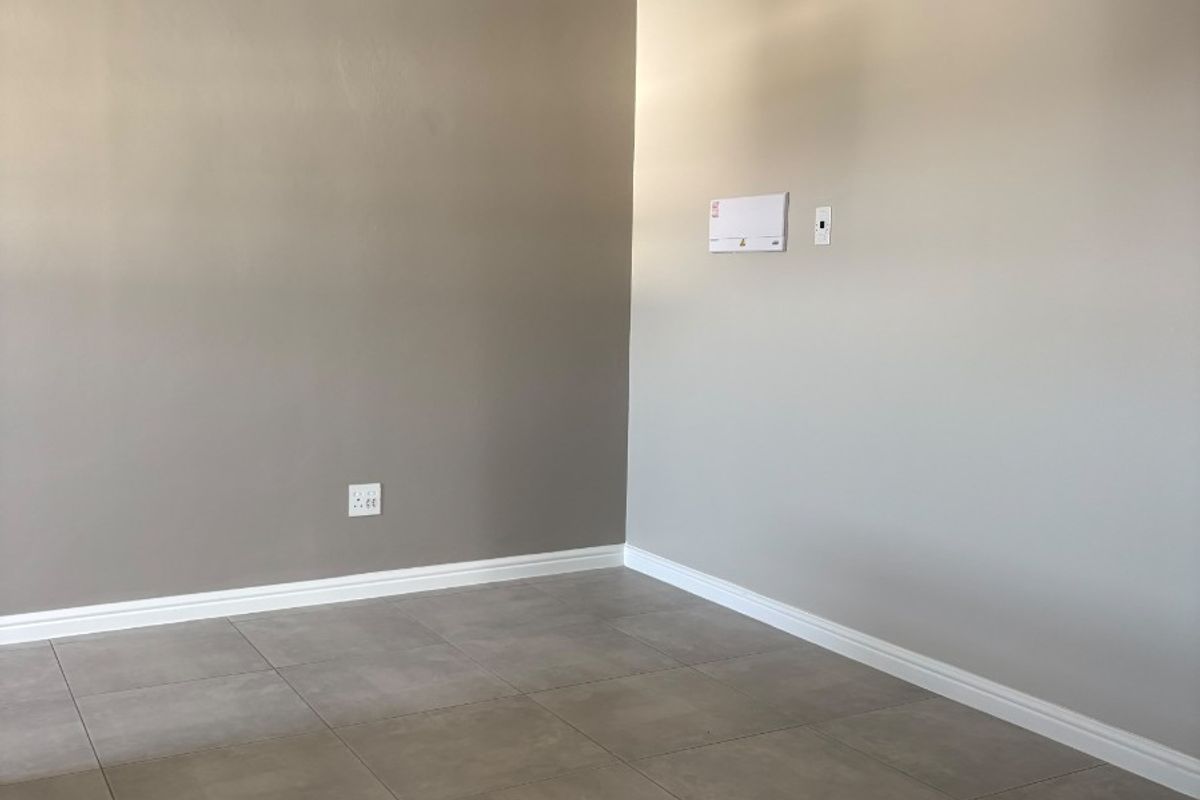 A clean, empty living area featuring neutral painted walls, modern grey floor tiles, and crisp white cornice detailing.