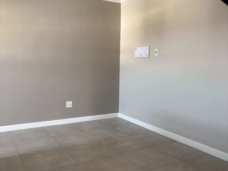 A clean, empty living area featuring neutral painted walls, modern grey floor tiles, and crisp white cornice detailing.