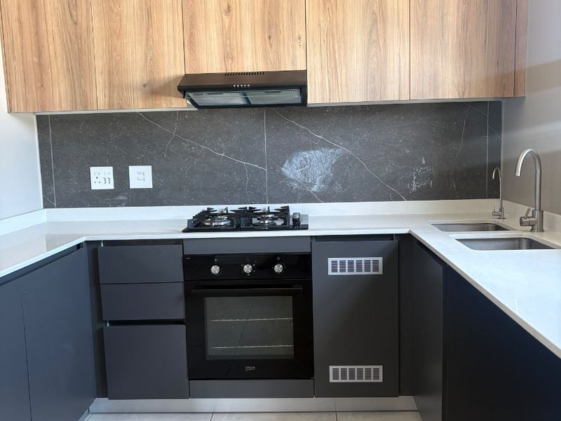 Modern kitchen featuring sleek dark cabinetry, stone countertops, integrated gas hob, built-in oven, and a stylish slatted timber feature wall.