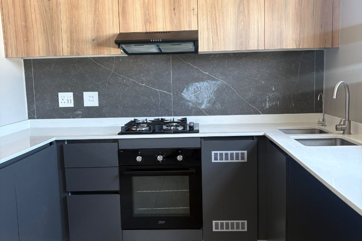 Modern kitchen featuring sleek dark cabinetry, stone countertops, integrated gas hob, built-in oven, and a stylish slatted timber feature wall.