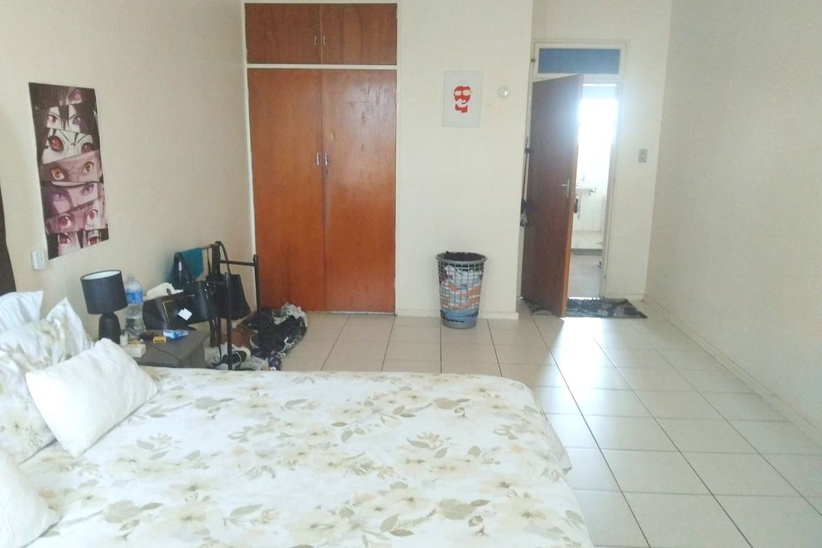 A bedroom featuring tiled flooring and a built-in wooden wardrobe, with an adjacent doorway leading to an en-suite bathroom.