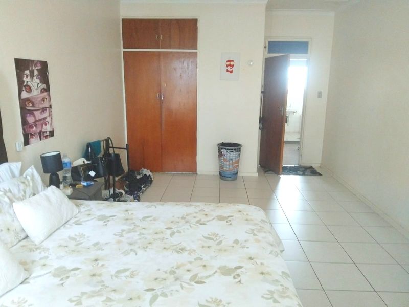 A bedroom featuring tiled flooring and a built-in wooden wardrobe, with an adjacent doorway leading to an en-suite bathroom.