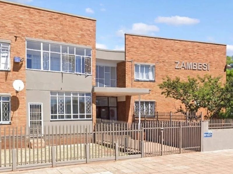 Front elevation of the Zambesi apartment complex featuring face brick construction, steel-framed windows with security bars, and secure perimeter fencing.