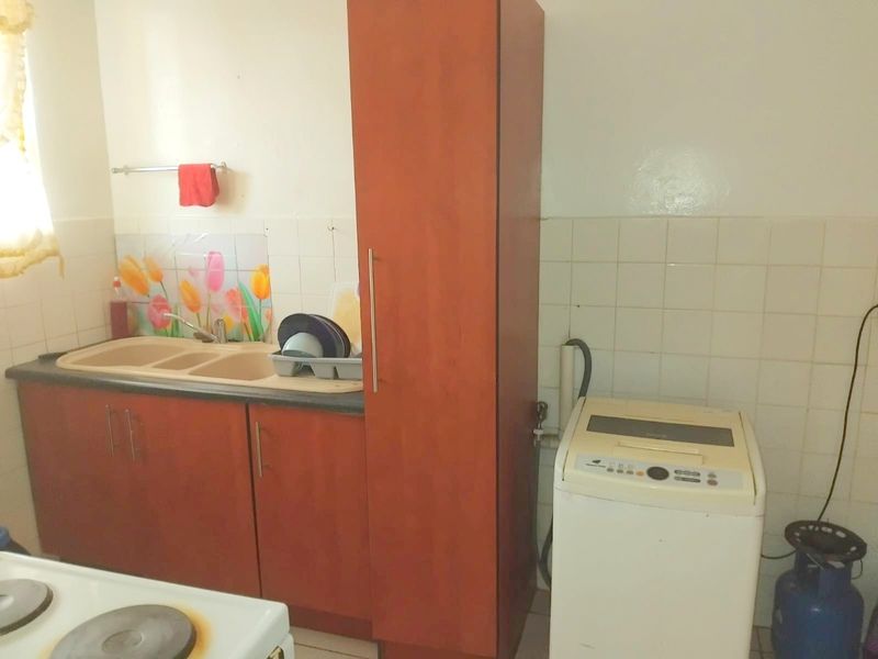 A compact kitchen area featuring built-in wooden cabinetry, a double sink, and tiled backsplash, offering functional storage and preparation space.