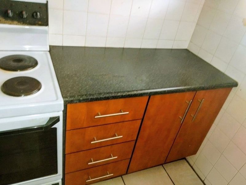 A functional kitchen area featuring wood-finish cabinetry, dark laminate countertops, and tiled splashbacks, providing a practical workspace for daily cooking needs.