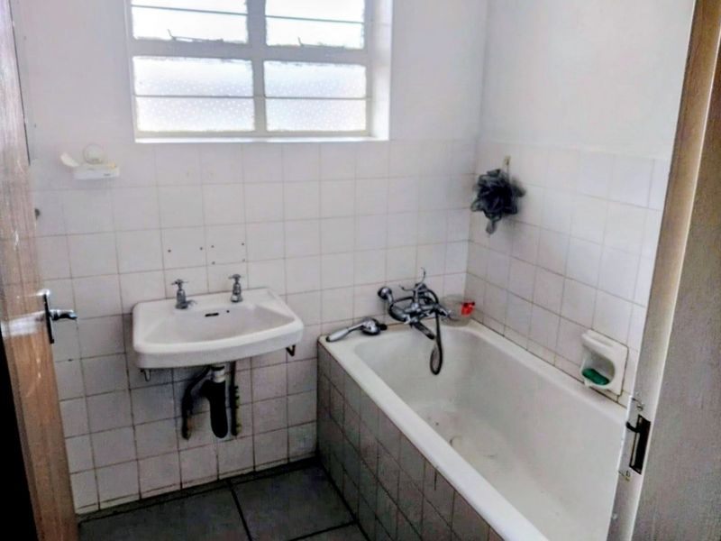 A dated bathroom featuring a wall-mounted basin, bathtub, and tiled finishes, requiring modernization and cosmetic updates to improve its overall condition and appeal.