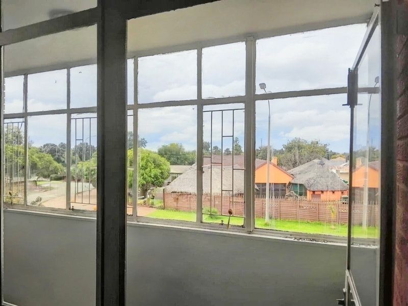 Enclosed balcony area featuring large steel-framed windows with security bars, offering an elevated view of the surrounding residential neighborhood.