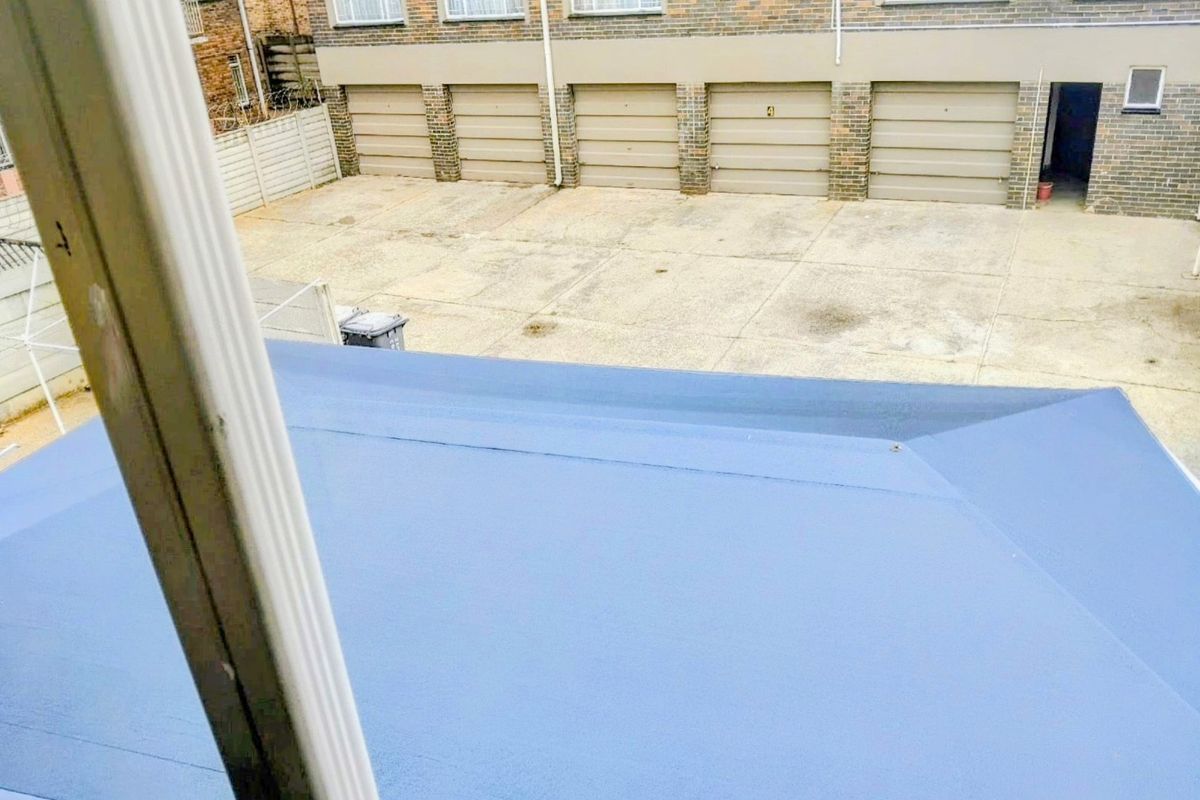 An elevated view of a rear courtyard area featuring a concrete driveway, multiple garage doors, and a brick building facade.