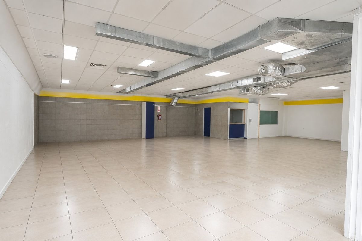 Spacious open-plan commercial area featuring tiled flooring, suspended ceilings with exposed HVAC ducting, and recessed lighting, suitable for retail or office use.