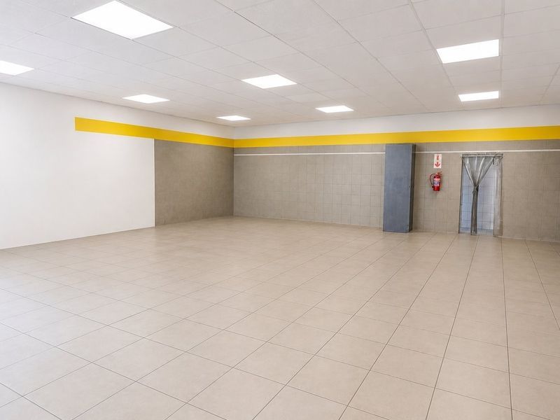 Spacious open-plan commercial area featuring neutral ceramic floor tiles, a suspended ceiling with recessed lighting, and durable tiled wall finishes.
