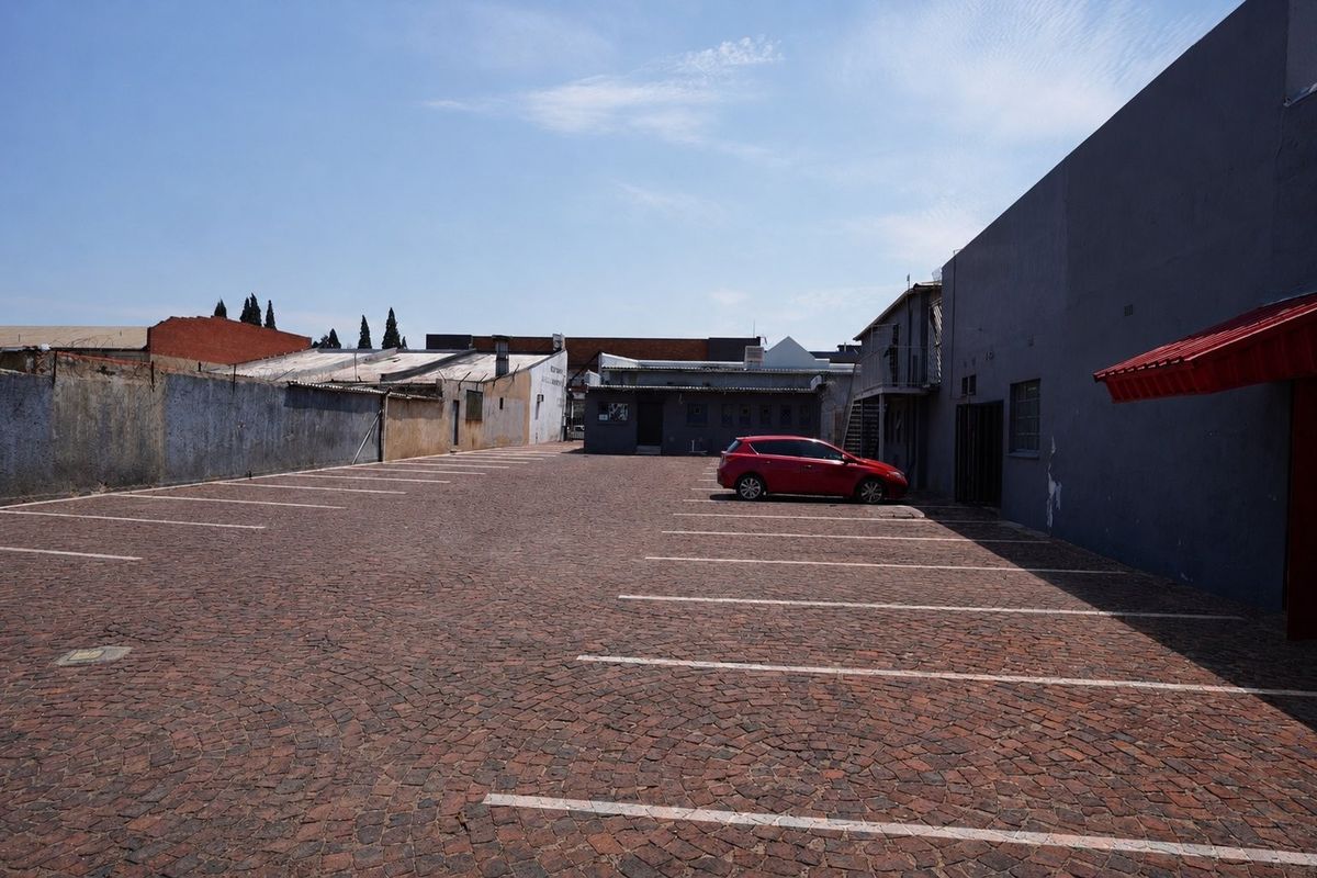 A paved commercial parking area featuring marked bays, perimeter masonry walls, and a metal awning attached to the building structure.