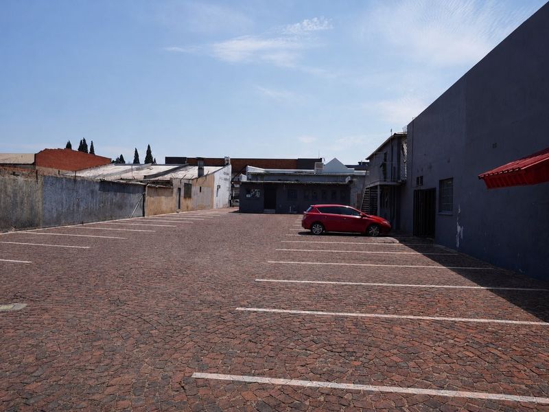 A paved commercial parking area featuring marked bays, perimeter masonry walls, and a metal awning attached to the building structure.