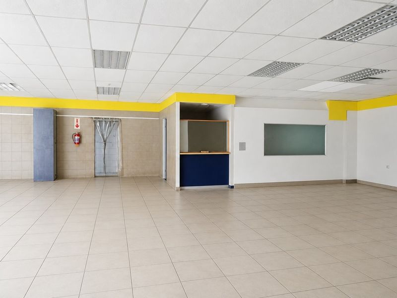 A spacious, open-plan commercial interior featuring neutral ceramic floor tiles, a suspended ceiling with recessed lighting, and a built-in service counter area.