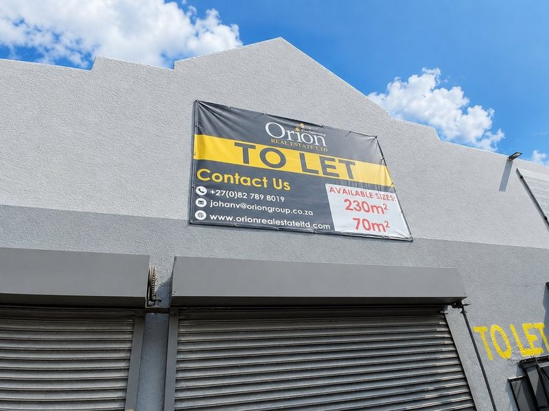 Exterior view of a commercial property featuring roller shutter doors and a prominent leasing sign on the textured facade.