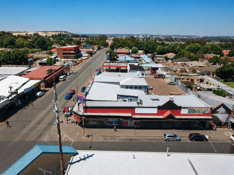 Aerial view of a commercial property featuring a metal roof, street-level storefronts, and an adjacent parking area in a suburban commercial district.