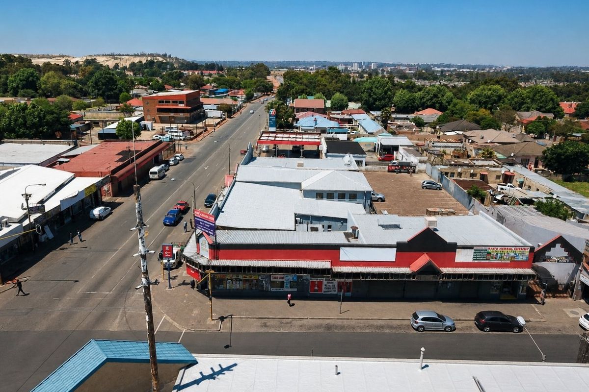 Aerial view of a commercial property featuring a metal roof, street-level storefronts, and an adjacent parking area in a suburban commercial district.