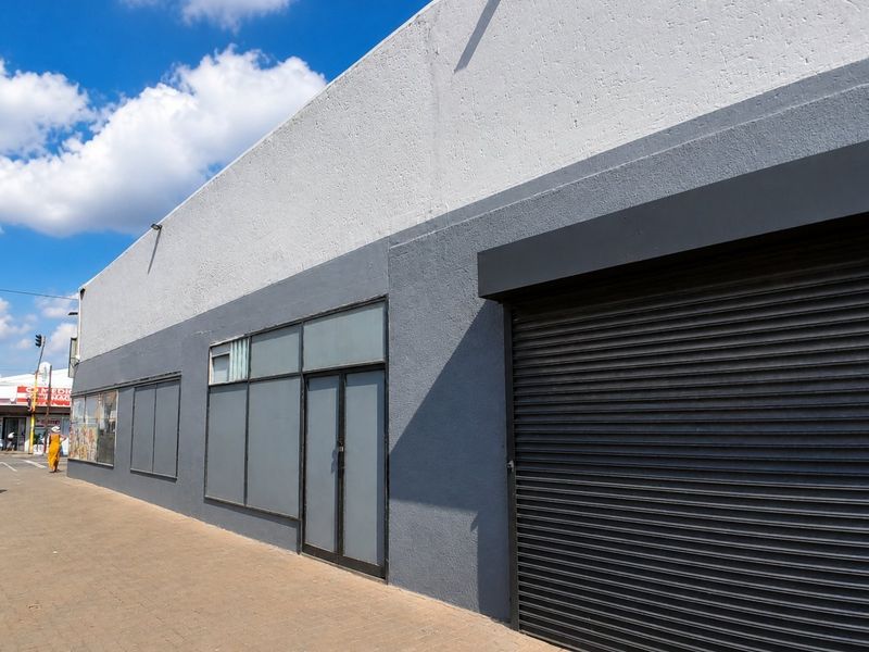 Commercial storefront featuring a modern grey facade, large glass windows, and a secure roller shutter door, situated along a paved street.